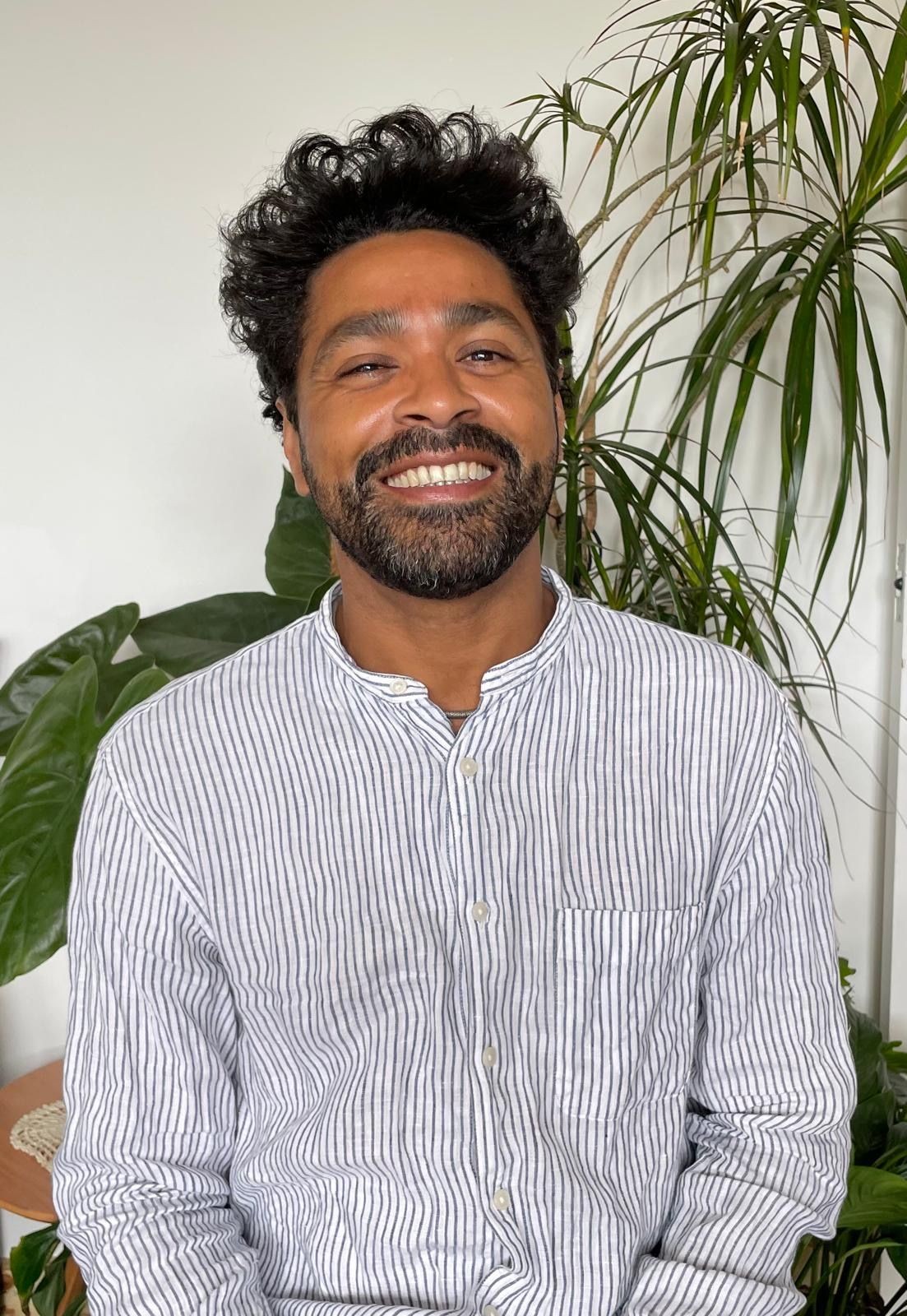 Smiling person in a striped shirt sitting with green plants in the background.